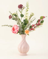 Le bouquet de fleurs artificielles en soie Pretty Petite, dans un vase rose pastel, contient des fleurs roses et orange faites à la main, des fleurs blanches, des feuilles vertes et des baies rouges - parfait pour un intérieur durable sur un fond clair uni.