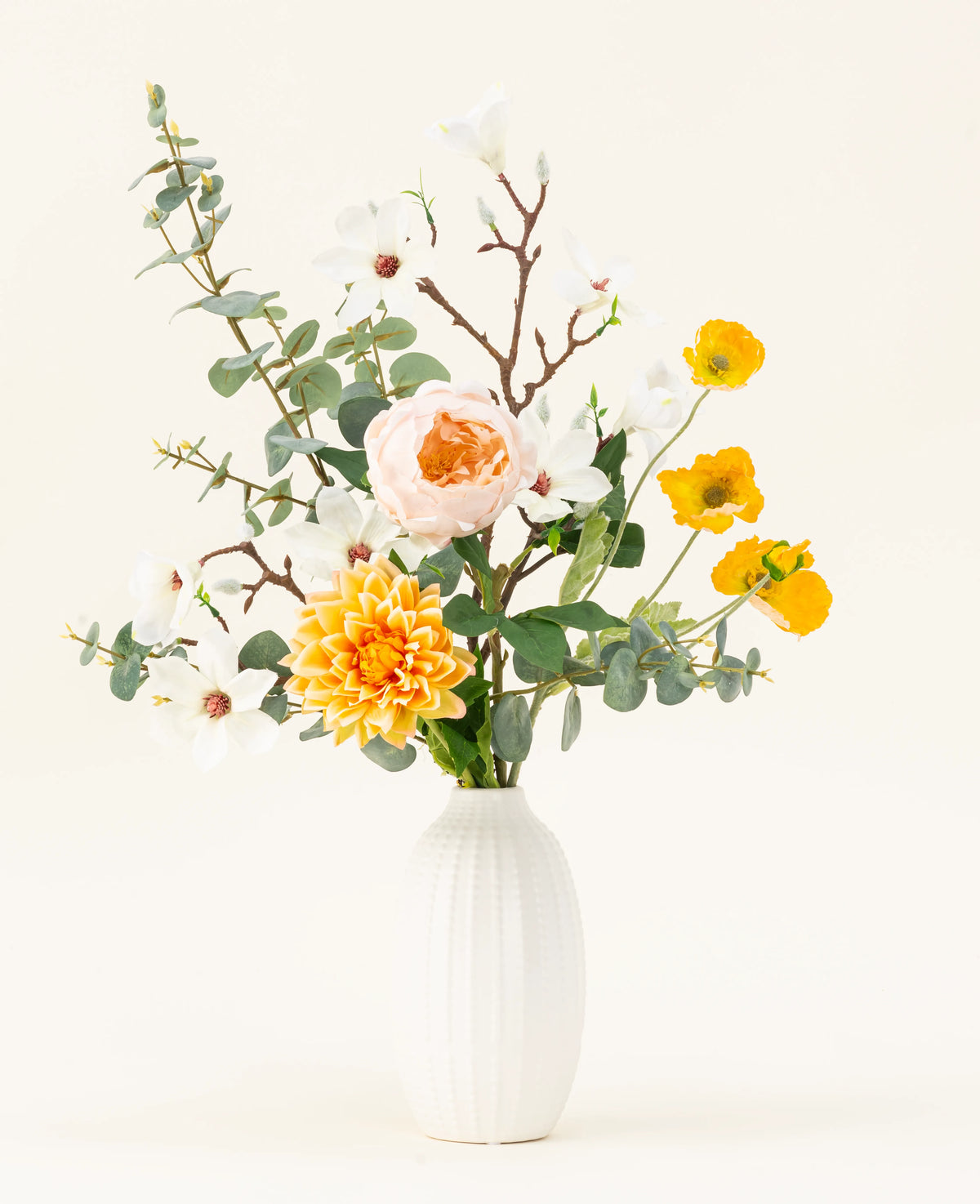 Le bouquet de fleurs artificielles en soie Fields of Joy présente des fleurs jaunes, blanches et pêche avec de l'eucalyptus vert dans un vase texturé blanc, joliment disposées sur un fond clair.