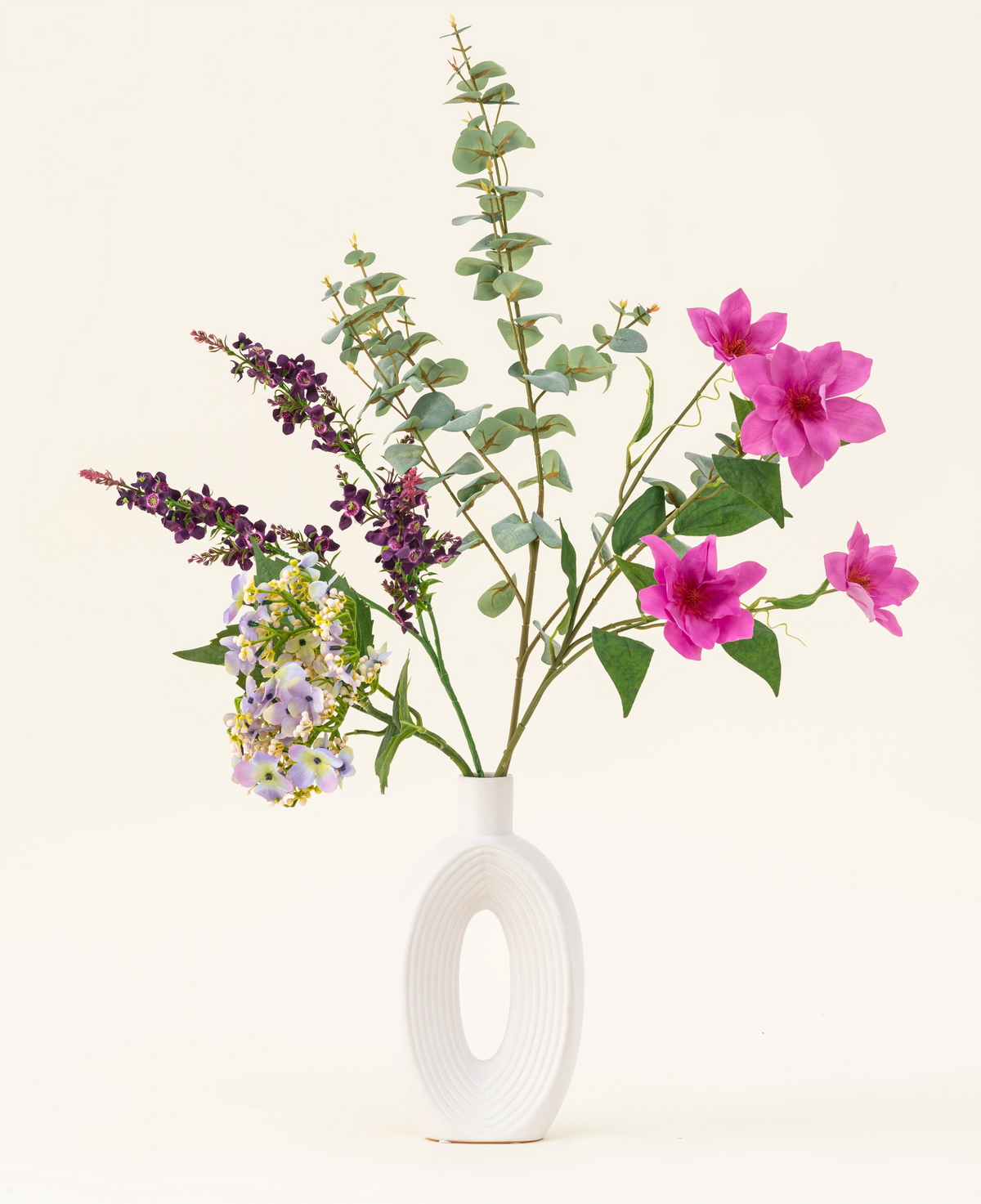 Disposé dans un vase blanc moderne, le bouquet de fleurs artificielles en soie Lavender Skies présente des fleurs artificielles roses et violettes, des accents jaunes et un feuillage vert luxuriant – magnifique sur un fond clair uni.