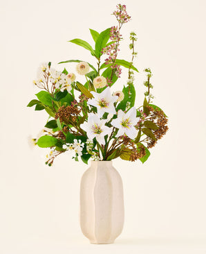 Bouquet de fleurs artificielles en soie Timeless Bloom, composé d'un bouquet de divers lys blancs, de petites fleurs blanches et de verdure dans un vase beige avec structure.
