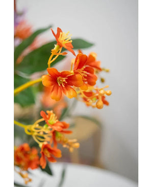 Gros plan de la branche artificielle Daphné Spray de 108 cm de couleur orange vif, avec des feuilles vertes réalistes et des étamines jaunes, sur un fond légèrement décoloré.