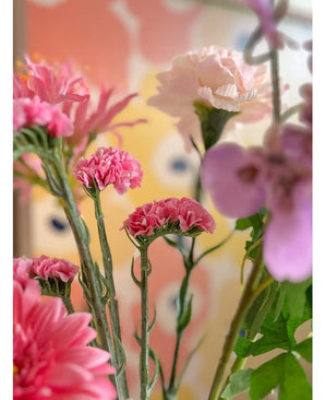 Un gros plan des fleurs artificielles roses Artificial Statice de 64 cm, avec de délicates fleurs de statice roses sur un fond pastel flou avec des formes abstraites jaunes et pêche.