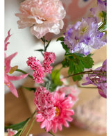 Un gros plan de la branche artificielle Statice 64 cm rose, avec de délicates fleurs de statice roses et des feuilles vertes, disposées en bouquet sur un fond intérieur légèrement décoloré.