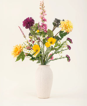 Het Zijden kunstbloemen boeket Daisy Daydream heeft een vaas met witte textuur en een levendige mix van gele, roze, paarse en witte bloemen met groene bladeren, die blijvende schoonheid toevoegt aan elke effen lichte achtergrond.