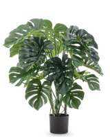 La plante artificielle Monstera 90 cm a de grandes feuilles vertes fendues et est présentée dans un pot noir sur un fond blanc uni.