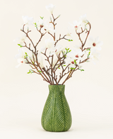 Un vase vert montre le bouquet de fleurs artificielles en soie Magnolia blanc, avec plusieurs branches de magnolia blanches avec de petites feuilles vertes, sur un fond clair uni.