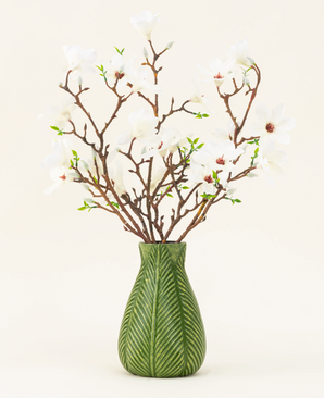 Un vase vert montre le bouquet de fleurs artificielles en soie Magnolia blanc, avec plusieurs branches de magnolia blanches avec de petites feuilles vertes, sur un fond clair uni.