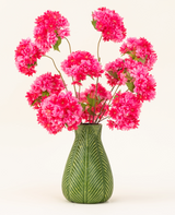 Un vase vert avec un motif de feuilles présente le bouquet de fleurs artificielles en soie Cherry Blossom Pink - des fleurs de cerisier en soie rose vif et moelleuses avec des feuilles vertes - sur un fond clair uni.