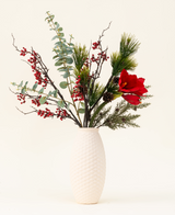 Het Zijden kunstbloemen boeket Winterberry Bliss heeft rode bessen, dennentakken, eucalyptus, rode amaryllis en dennenappels in een witte vaas met textuur - ideaal voor kerstdecoratie of om te laten zien tegen een lichte achtergrond.