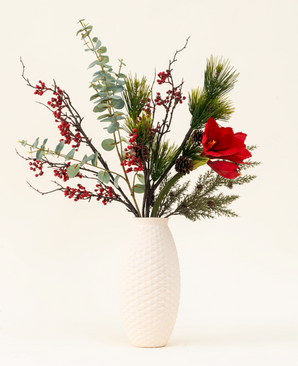 Het Zijden kunstbloemen boeket Winterberry Bliss heeft rode bessen, dennentakken, eucalyptus, rode amaryllis en dennenappels in een witte vaas met textuur - ideaal voor kerstdecoratie of om te laten zien tegen een lichte achtergrond.