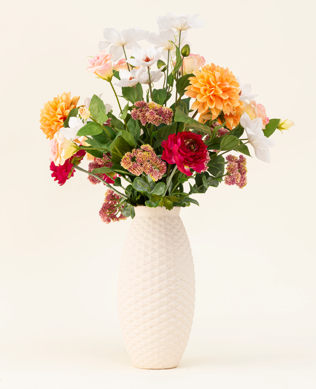Le bouquet de fleurs artificielles en soie The Wild Bunch, avec des roses rouges, du Dahlia Real Touch, des fleurs roses et des feuilles vertes dans un vase structuré blanc, est présenté sur un fond clair.