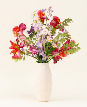 In een vaas met witte structuur staat het Zijden kunstbloemen boeket Pink Pop, met levendige kunstroze bloemen en groene bladeren tegen een lichte achtergrond.