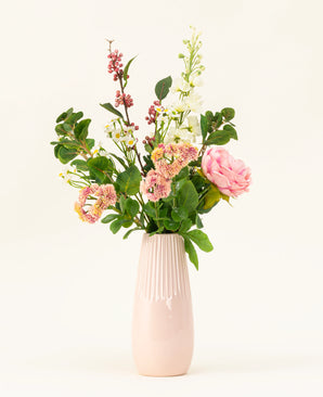 Een roze vaas van keramiek toont het Zijden kunstbloemen boeket Daisy Charm, met verschillende bloemen en groen - roze rozen, witte bloesems en rode bessen - prachtig gerangschikt tegen een effen lichte achtergrond.