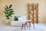 Salon minimaliste avec un canapé blanc, deux coussins, des tables gigognes en bois et une grande Plante Artificielle Strelitzia Real Touch Deluxe 180 cm pour une ambiance tropicale. Une bibliothèque ouverte moderne en bois avec des vases se dresse contre le mur beige.