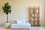 Minimalistische woonkamer met een witte bank, twee kussens en een Kunstplant Ficus Tabaksplant Deluxe 180 cm naast een open houten plank met witte vazen, alles tegen een beige muur en op een licht vloerkleed.