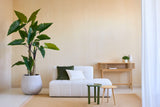 Un salon minimaliste avec la plante Artificielle Calocasia 210 cm, un canapé texturé blanc avec des coussins verts et blancs, deux petites tables d'appoint, un tapis beige et une console en bois contre un mur beige clair.