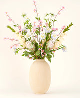 In een vaas met beige structuur staat het Zijden kunstbloemen boeket Lots of Love XL, een handgebonden boeket van roze, witte en blauwe zijden bloemen met groene bladeren en lange stelen tegen een lichte achtergrond.