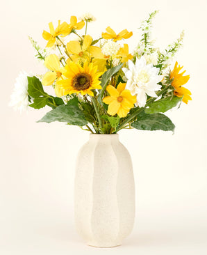 Le bouquet de fleurs artificielles en soie Sunny Whisper, composé de tournesols, de dahlias blancs et de feuilles vertes dans un vase en céramique beige, se détache magnifiquement sur un fond clair.