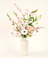 Un vase de couleur crème montre le bouquet de fleurs artificielles en soie Pink & Pearl, avec de délicates fleurs en soie roses, blanches et pêche avec des feuilles vertes sur un fond neutre clair.