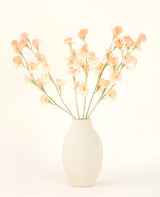 Le vase en céramique de couleur crème contient le bouquet de fleurs artificielles Silk Pea Peach, avec de délicates fleurs pêche et rose clair avec de longues tiges vertes sur un fond clair et neutre.
