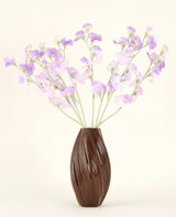Un vase marron texturé contient le bouquet de fleurs artificielles en soie, des fleurs en soie violet-violet clair avec des tiges verdâtres sur un fond uni et clair.