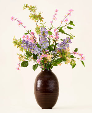Dans un vase marron foncé se trouve un bouquet de fleurs artificielles en soie roses, violettes et jaunes, le bouquet « Sky Kiss », avec des feuilles vertes, sur un fond uni clair. Cette décoration sans entretien apporte une beauté durable à n'importe quelle pièce, sans nécessiter d'entretien.