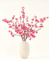 Le bouquet de fleurs artificielles en soie Fleur de cerisier fuchsia 150 cm présente des tiges de fleurs de cerisier fuchsia vibrantes avec des feuilles vertes dans un simple vase blanc, qui complètera n'importe quel intérieur sur un fond clair.