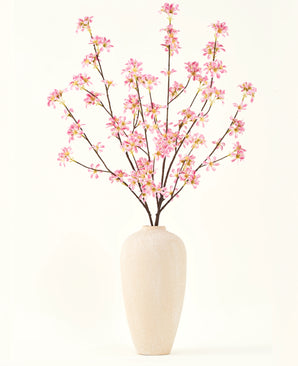 Un grand vase en céramique beige contient plusieurs branches du bouquet de fleurs artificielles en soie. Fleurs roses, avec de délicates fleurs roses et des feuilles vertes, sur un fond blanc uni.