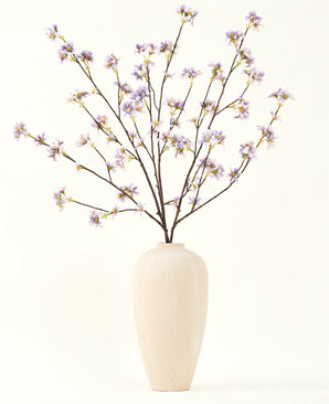 Un grand vase en céramique de couleur crème contient un certain nombre de fines branches avec le texte Bouquet de fleurs artificielles en soie Branche de fleurs artificielles violette, sur un fond uni et clair.