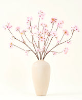 Le bouquet de fleurs artificielles en soie Fleur de cerisier rose 114 cm a des branches longues et fines avec des bouquets de fleurs rose clair dans un vase en céramique beige, qui forment un contraste saisissant sur le fond blanc uni.