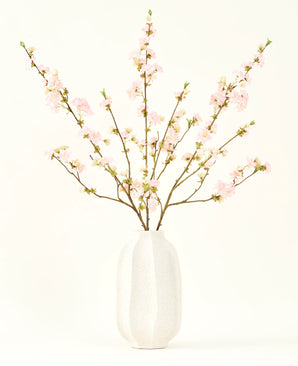 Le bouquet de fleurs artificielles en soie Fleur de cerisier rose clair 94 cm présente de délicates fleurs de cerisier artificielles roses dans un vase en céramique blanche, qui ajoute de l'élégance sur un fond clair et uni.