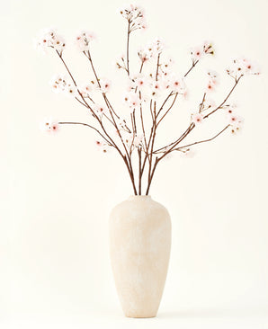 Le bouquet de fleurs artificielles en soie Cherry Blossom Blush 114 cm présente des branches hautes et délicates dans un vase beige sobre, qui apportera une touche douce et élégante à votre intérieur sur un fond uni et clair.