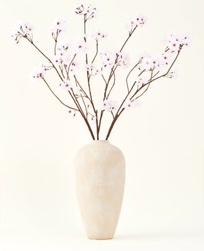 Le bouquet de fleurs artificielles en soie Fleur de cerisier rose clair 114 cm se dresse dans un grand vase en céramique beige avec de longues et fines branches et de délicates fleurs rose clair, créant un accent floral artificiel serein sur un fond uni.