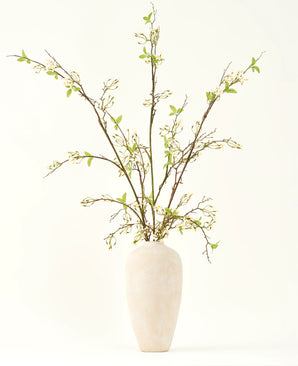 Un grand vase en céramique de couleur crème contient le bouquet de fleurs artificielles en soie Verveine crème avec de longues branches, de petites feuilles vertes et de délicates fleurs blanches, joliment disposées sur un fond clair et uni.