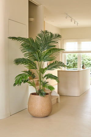 Une plante artificielle Chamaedorea de 180 cm se dresse dans une cuisine moderne et lumineuse avec des tons neutres, une décoration minimaliste et une lumière naturelle entrant par les fenêtres.