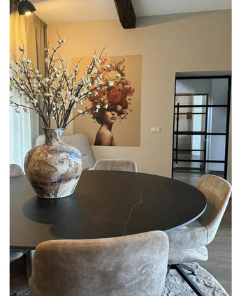 Un coin repas moderne avec une table ronde noire, des chaises beiges et un grand vase en céramique avec fleur de cerisier japonais artificielle de 94 cm blanche. Une fresque murale représentant une femme avec des fleurs dans les cheveux décore le fond.