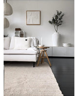 Een minimalistische woonkamer met een lichtgekleurde bank, neutraal vloerkleed, wit dressoir, Kunst Olijfboom 120 cm als decoratief element, abstracte muurkunst en houten krukjes-alles in zachte Mediterrane sfeer met neutrale tinten.