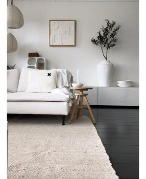 Een minimalistische woonkamer met een lichtgekleurde bank, neutraal vloerkleed, wit dressoir, Kunst Olijfboom 120 cm als decoratief element, abstracte muurkunst en houten krukjes-alles in zachte Mediterrane sfeer met neutrale tinten.