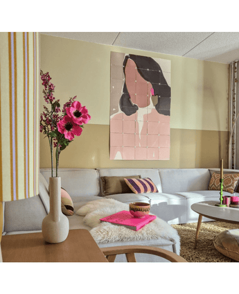 Un salon cosy avec un canapé gris clair, des accents roses et dorés, une fleur artificielle d'anémone ramifiée de 56 cm rose dans un vase moderne, une table basse avec un tapis en fourrure et un art abstrait pastel représentant une femme au mur.