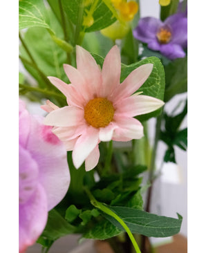 Een close-up van de Kunstbloem Aster 60 cm roze bloemblaadjes met een geel hart, omringd door groene bladeren en andere bloemen, waaronder een paarse, op de achtergrond.