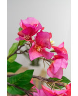 Gros plan de la Fleur Artificielle Bougainvillier 90 cm violet : fleurs de bougainvilliers artificielles violet vif avec des feuilles vertes sur une branche, sur un fond doux et clair.