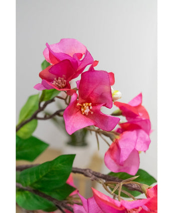 Gros plan de la Fleur Artificielle Bougainvillier 90 cm violet : fleurs de bougainvilliers artificielles violet vif avec des feuilles vertes sur une branche, sur un fond doux et clair.