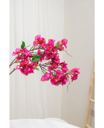 La fleur artificielle Bougainvillier 90 cm violet, avec des fleurs violettes vibrantes et des feuilles vertes, est présentée sur un fond neutre clair à côté d'une échelle en bois à droite.