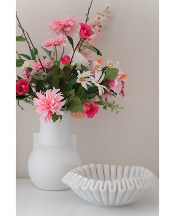 Un vase blanc avec une fleur artificielle Rhododendron Azalea 73 cm fuchsia se trouve à côté d'un bol blanc en céramique nervurée sur une surface unie sur un fond neutre.