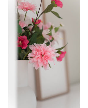 Un gros plan de la fleur artificielle Dahlia 68 cm rose dans un vase blanc, avec un léger cadre photo en arrière-plan sur une surface blanche.