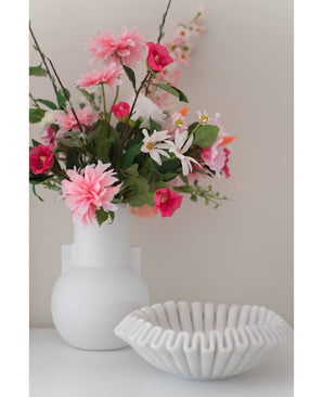 Une fleur artificielle Dahlia de 68 cm rose dans un vase blanc se trouve à côté d'un bol en céramique blanche avec des volants sur une surface blanche, sur un fond uni clair.