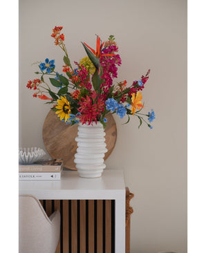 Un vase blanc texturé contient un bouquet rose d'herbe à chat artificielle de 75 cm sur une table blanche à côté de livres empilés et de décorations, avec un plateau rond en bois appuyé contre le mur beige en arrière-plan.
