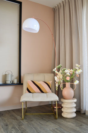 Un coin moderne et cosy avec une chaise couleur crème avec un coussin rayé, un grand lampadaire en forme d'arc, des rideaux beiges, un parquet et un vase rond avec des fleurs artificielles Fritillary 94 cm blanches sur une table d'appoint sculptée.