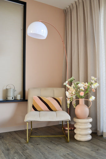 Un coin moderne et cosy avec une chaise couleur crème avec un coussin rayé, un grand lampadaire en forme d'arc, des rideaux beiges, un parquet et un vase rond avec des fleurs artificielles Fritillary 94 cm blanches sur une table d'appoint sculptée.