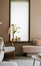Un salon cosy avec des murs rose clair, une grande fenêtre avec un store enrouleur blanc, des canapés crème et blush et une chaise en bois avec la fleur artificielle fritillaire 94 cm blanche à côté d'objets décoratifs sur le rebord de la fenêtre.